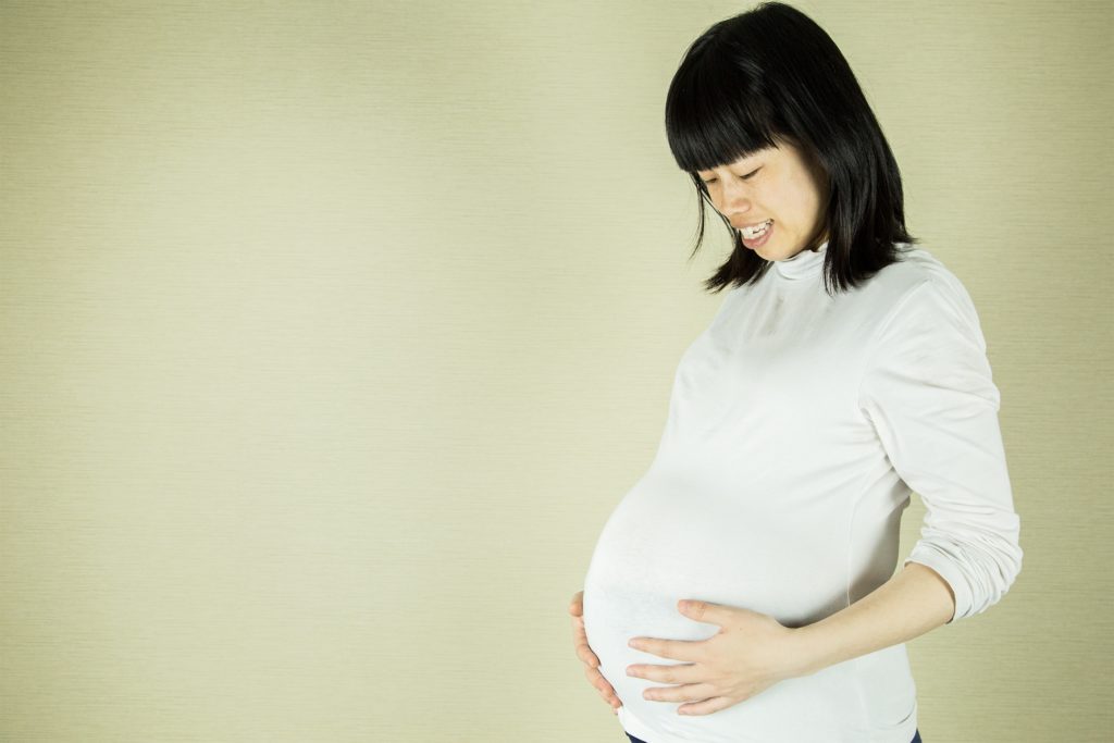 Pregnant woman in white top against cream background