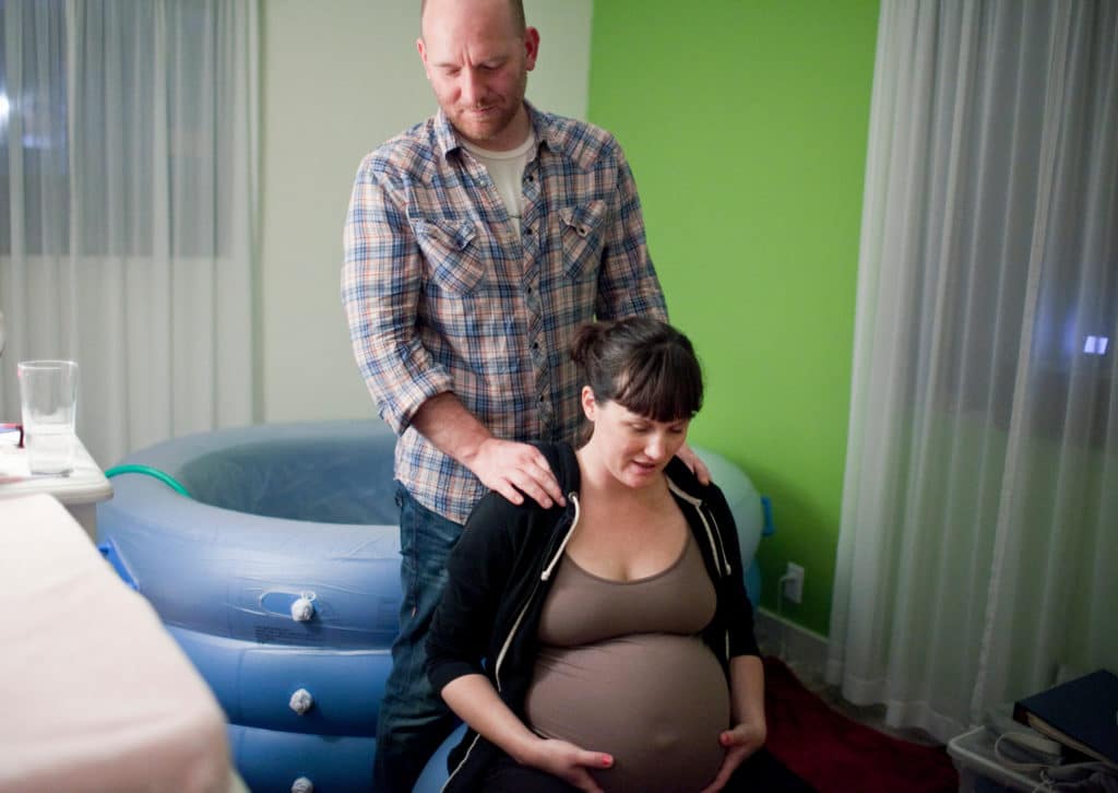 Spouse supporting pregnant woman in labour by massaging her shoulders