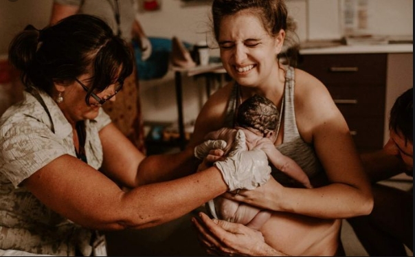 Midwife helps mother lift her just-born baby to her chest.